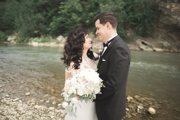 Κομψή κομψό ευτυχισμένη μελαχρινή νύφη και ο γαμπρός πανέμορφο στο φόντο της ένα πανέμορφο καταρράκτη στα βουνά — Φωτογραφία Αρχείου