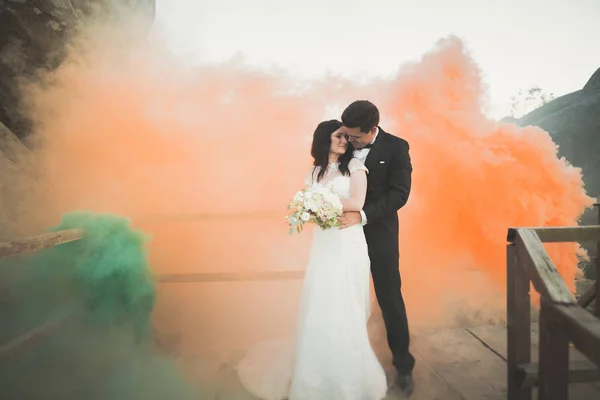 Casamento casal posando perto de pedras com fumaça colorida atrás deles — Fotografia de Stock