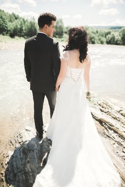 Bellissimo matrimonio coppia baciare e abbracciare vicino alla riva di un fiume di montagna con pietre — Foto Stock