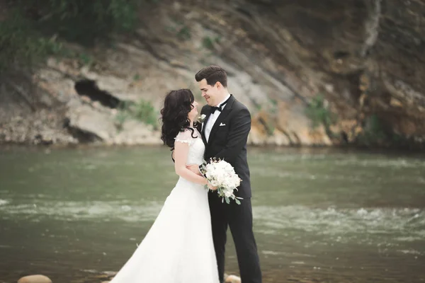 Magnifique couple de mariage embrasser et embrasser près de la rive d'une rivière de montagne avec des pierres — Photo