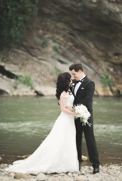 Elegante elegante novia morena feliz y magnífico novio en el fondo de una hermosa cascada en las montañas —  Fotos de Stock