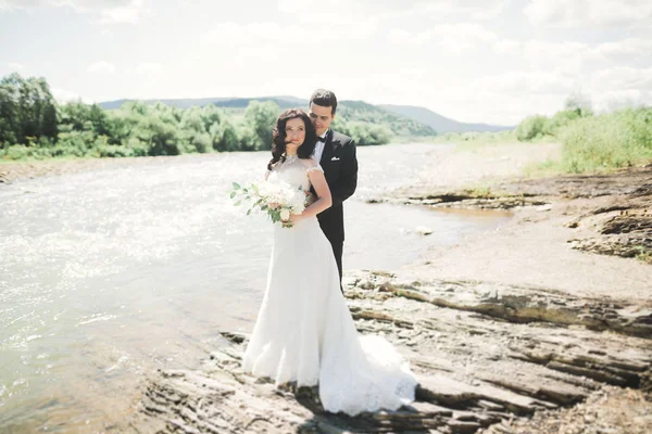 Красива весільна пара цілується і обіймається біля берега гірської річки з камінням — стокове фото