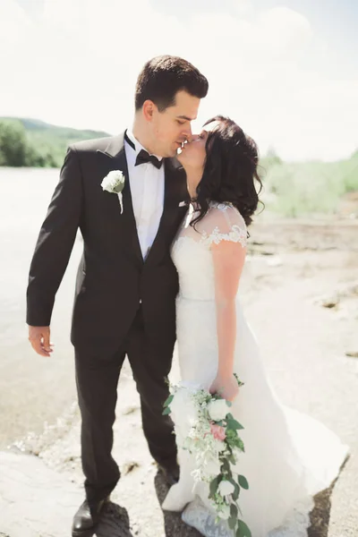 Όμορφος γάμος ζευγάρι φιλιά και αγκαλιάζει κοντά στην ακτή ενός ποταμού βουνό με πέτρες — Φωτογραφία Αρχείου