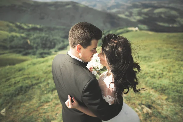 Schöne fabelhafte glückliche Braut und stilvoller Bräutigam posiert auf dem Hintergrund der sonnigen atemberaubenden Berge — Stockfoto