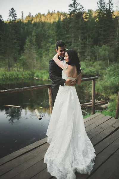 Encantadora novia, elegante novio en paisajes de montañas y puesta de sol en el lago. Hermosa pareja de boda —  Fotos de Stock