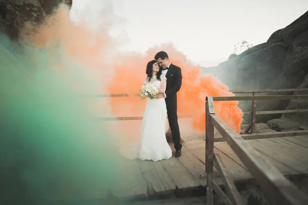 Couple de mariage posant près des rochers avec de la fumée colorée derrière eux — Photo