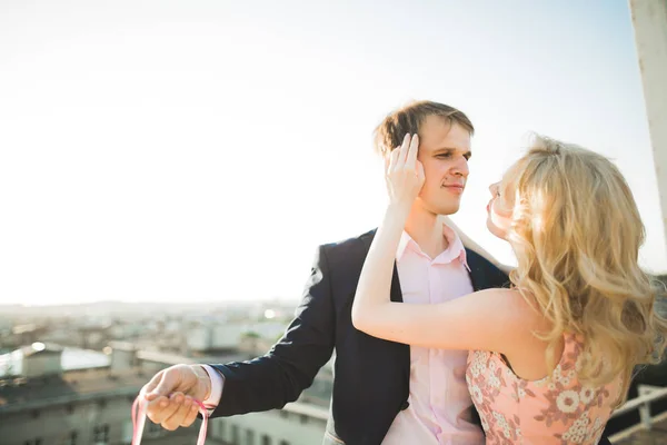 Jovem casal apaixonado posando no telhado com vista perfeita da cidade de mãos dadas e abraços. Belo pôr do sol — Fotografia de Stock