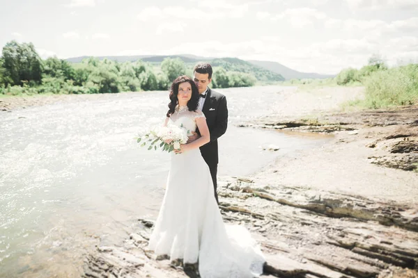 Елегантна стильна щаслива брюнетка наречена і чудовий наречений на тлі красивого водоспаду в горах — стокове фото