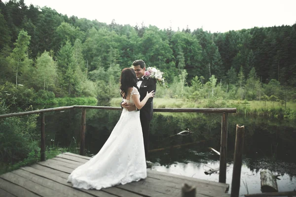 Encantadora novia, elegante novio en paisajes de montañas y puesta de sol en el lago. Hermosa pareja de boda —  Fotos de Stock