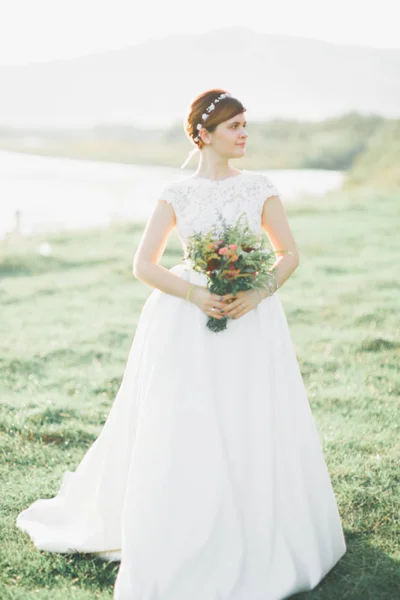 Novia en vestido de novia posando sobre hierba con hermoso paisaje de fondo — Foto de Stock