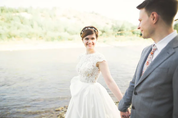 新娘和新郎抱着美丽的婚礼花束。河边摆姿势 — 图库照片