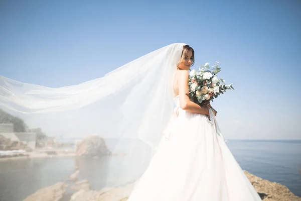 Bella giovane sposa con bouquet da sposa in posa sullo sfondo mare — Foto Stock