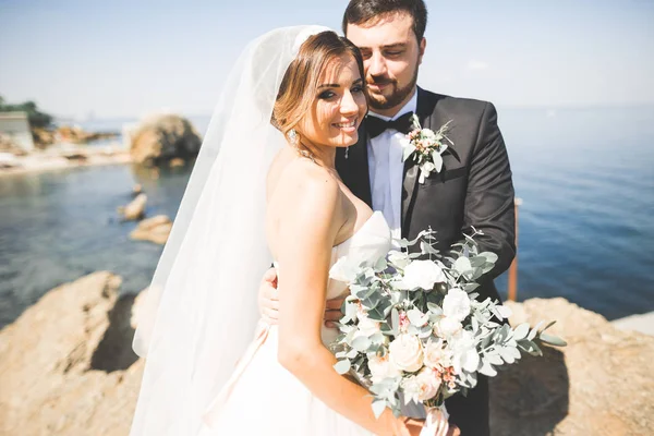 Boda pareja, novio, novia con ramo posando cerca del mar y el cielo azul —  Fotos de Stock