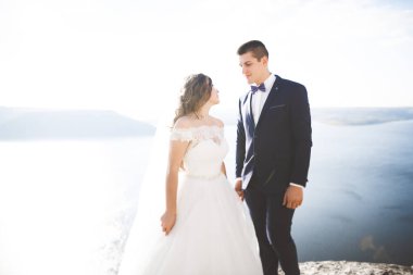 Düğün çifti mavi denizin yanındaki kayalarda öpüşüyor ve sarılıyor.