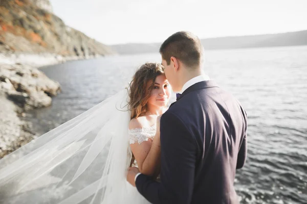 Elegant, stilig, lykkelig ektepar, brud, nydelig brudgom i bakgrunnen av hav og himmel – stockfoto