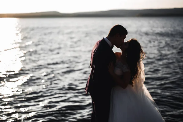 Boda pareja besándose y abrazándose en rocas cerca de mar azul —  Fotos de Stock