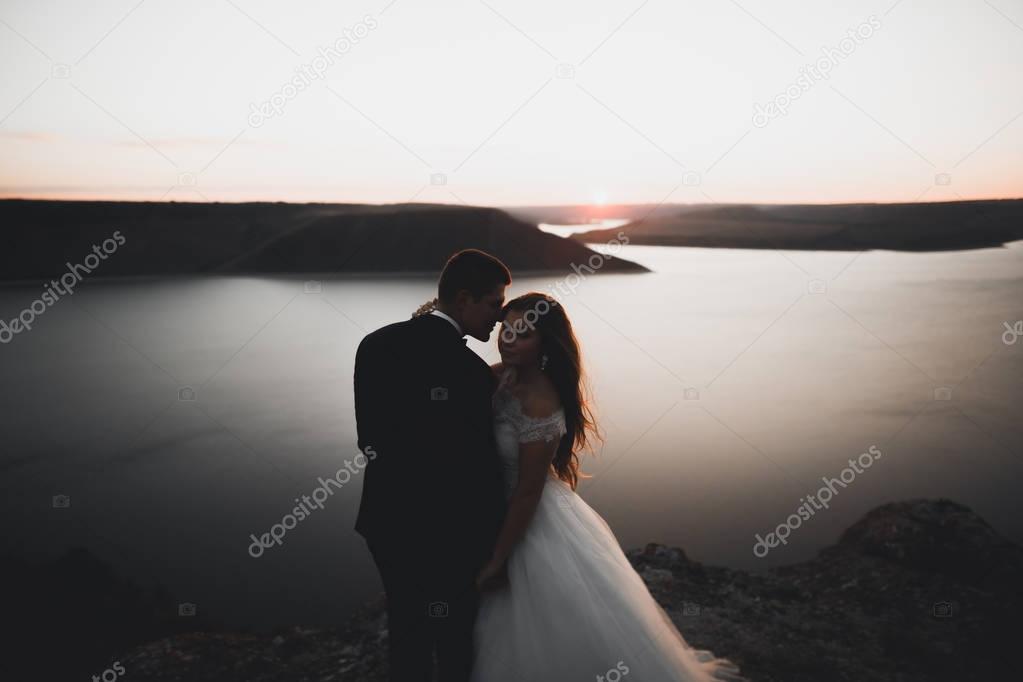 Wedding couple, groom, bride posing near sea on sunset