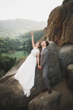 Yeni evli çift, gelin ve damat öpüşüyor, mükemmel dağ manzarasında sarılıyorlar, mavi gökyüzü