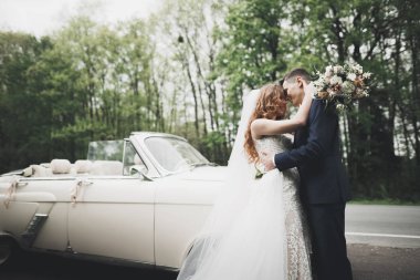 Şık bir düğün çifti, gelin, damat retro arabada öpüşüyor ve sarılıyor.