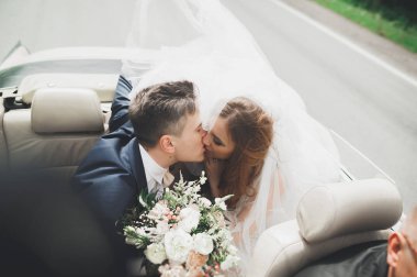 Şık bir düğün çifti, gelin, damat retro arabada öpüşüyor ve sarılıyor.