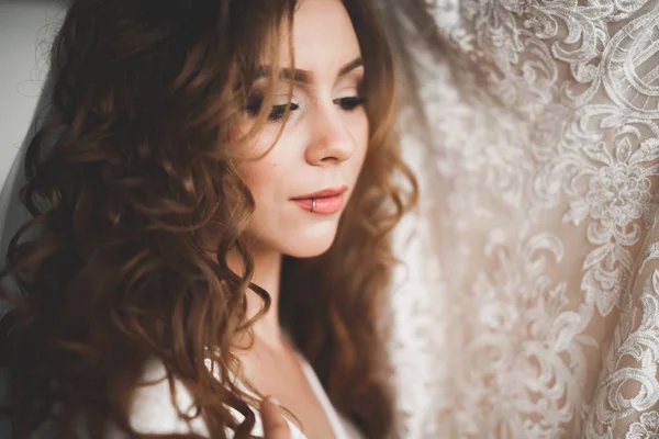 Preciosa novia en bata posando y preparándose para la ceremonia de boda cara en una habitación — Foto de Stock