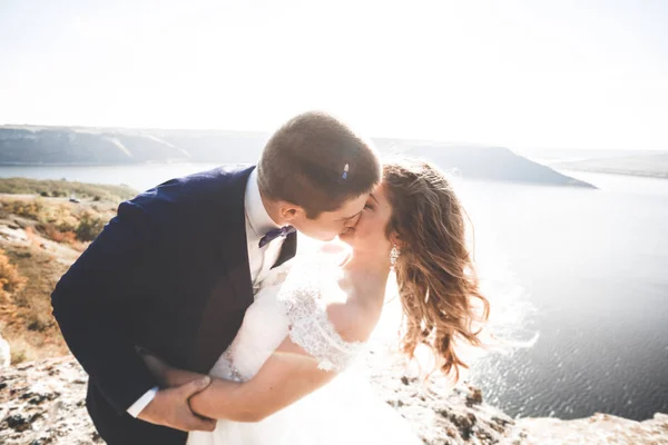 Свадебная пара целуется и обнимается на скалах у синего моря — стоковое фото