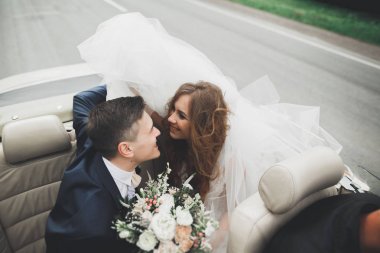 Şık bir düğün çifti, gelin, damat retro arabada öpüşüyor ve sarılıyor.