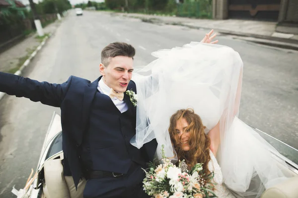 Şık bir düğün çifti, gelin, damat retro arabada öpüşüyor ve sarılıyor. — Stok fotoğraf