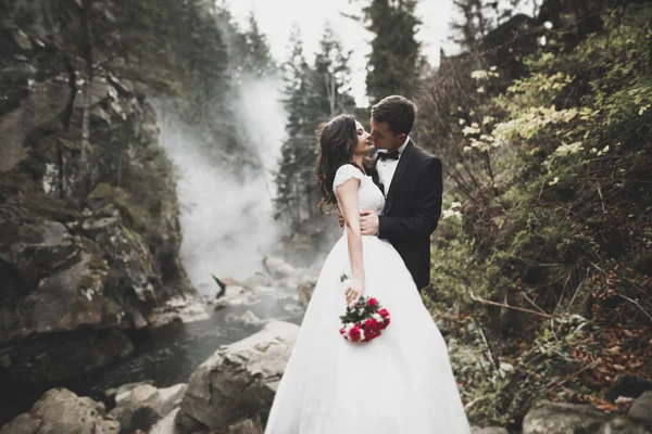 Elegante stilvolle glücklich brünette Braut und wunderschöner Bräutigam auf dem Hintergrund eines schönen Flusses in den Bergen — Stockfoto