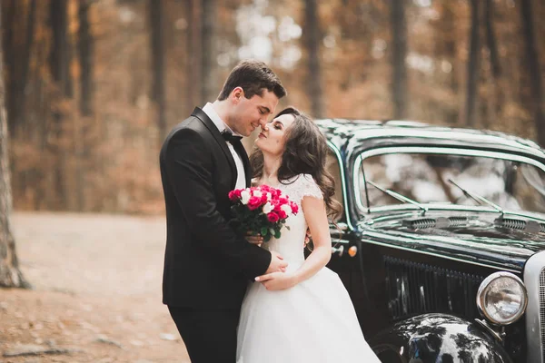Stijlvol bruidspaar, bruid, bruidegom kussen en knuffelen op retro auto — Stockfoto