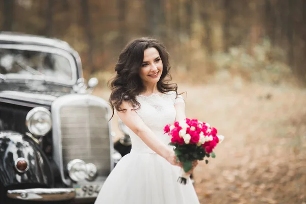 Hermosa novia en elegante vestido blanco sosteniendo ramo posando en el parque —  Fotos de Stock