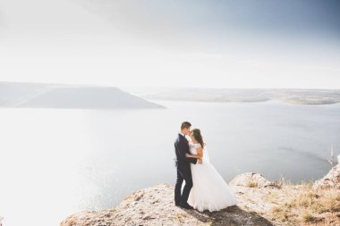 Şık, şık, mutlu bir düğün çifti, gelin, deniz ve gökyüzünün arka planında muhteşem bir damat.