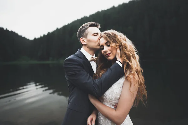 Młoda para nowożeńców, narzeczona i pan młody całujący się, przytulający się na doskonały widok na góry, błękitne niebo — Zdjęcie stockowe