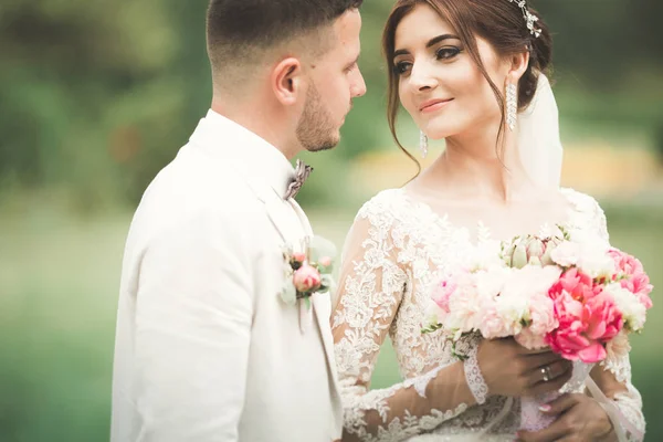 Casal elegante de recém-casados felizes andando no parque em seu dia de casamento com buquê — Fotografia de Stock