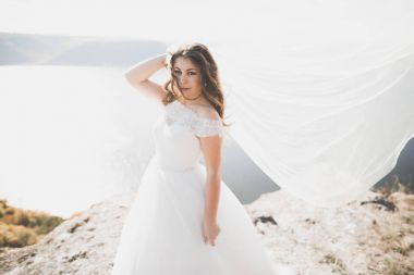 Güzel bayan, gelin gün batımında deniz kenarında bir gelinlik içinde poz veriyor.