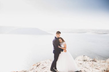 Şık, şık, mutlu bir düğün çifti, gelin, deniz ve gökyüzünün arka planında muhteşem bir damat.