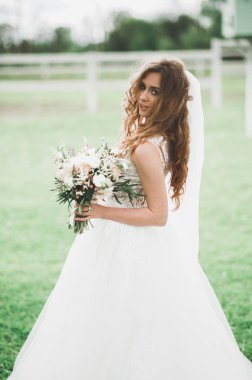 Çekici gelinin portresi, uzun saçlı, büyük buketli poz veren.