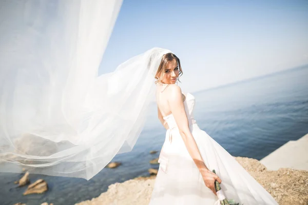 Krásná mladá nevěsta s svatební kytice pózuje na pozadí moře — Stock fotografie