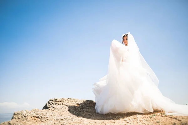 Preciosa novia en vestido de novia blanco posando cerca del mar con hermoso fondo —  Fotos de Stock