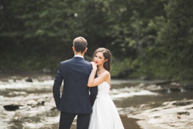 Zarif nazik şık damat ve gelin taşlarla Nehri yakınında. Evlilik çift aşık