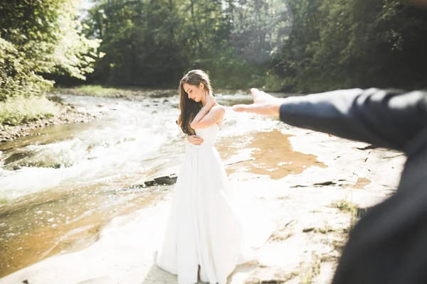 Güzel düğün çifti bir dağ nehrinin kıyısında taşlarla öpüşüp kucaklaşıyorlar. — Stok fotoğraf