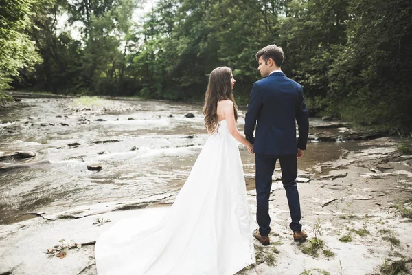 Elegante stijlvolle gelukkig brunette bruid en prachtige bruidegom op de achtergrond van een mooie rivier in de bergen — Stockfoto