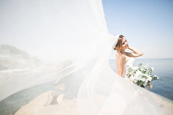 Bella sposa in abito da sposa bianco in posa vicino al mare con bellissimo sfondo — Foto Stock