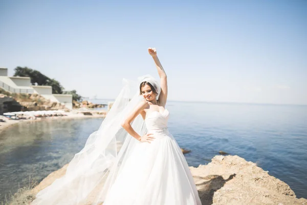 Preciosa novia en vestido de novia blanco posando cerca del mar con hermoso fondo —  Fotos de Stock