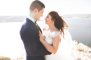 Düğün çifti mavi denizin yanındaki kayalarda öpüşüyor ve sarılıyor.