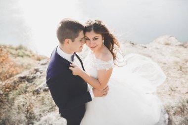 Şık, şık, mutlu bir düğün çifti, gelin, deniz ve gökyüzünün arka planında muhteşem bir damat.