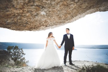 Şık, şık, mutlu bir düğün çifti, gelin, deniz ve gökyüzünün arka planında muhteşem bir damat.