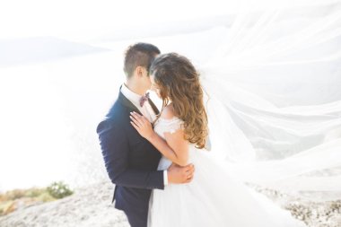 Düğün çifti mavi denizin yanındaki kayalarda öpüşüyor ve sarılıyor.