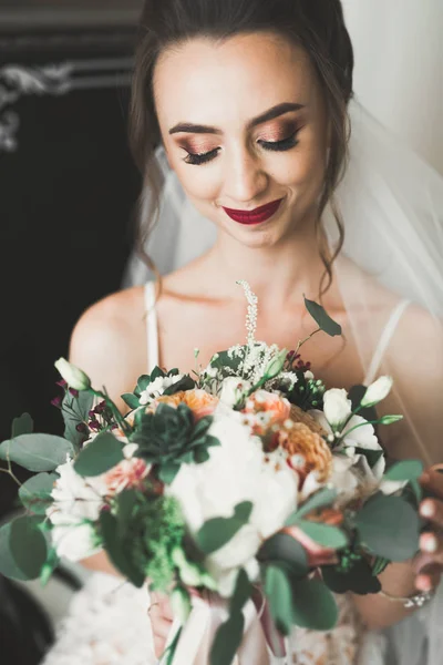 Preciosa novia en bata posando y preparándose para la ceremonia de boda cara en una habitación —  Fotos de Stock