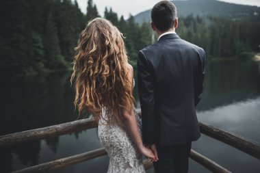 Yeni evli çift, gelin ve damat öpüşüyor, mükemmel dağ manzarasında sarılıyorlar, mavi gökyüzü